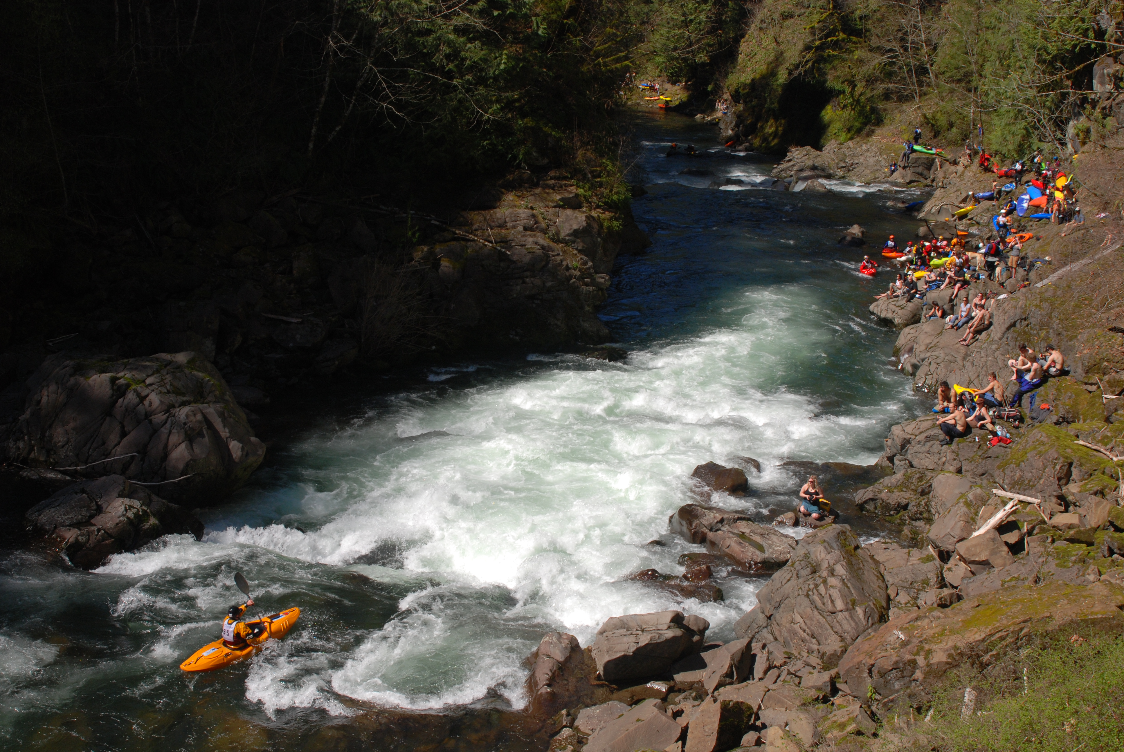 Kayaker running the final drop at the finish of the 2008 Canyon Creek Whitewater Race as spectators watch from shoreline rocks.