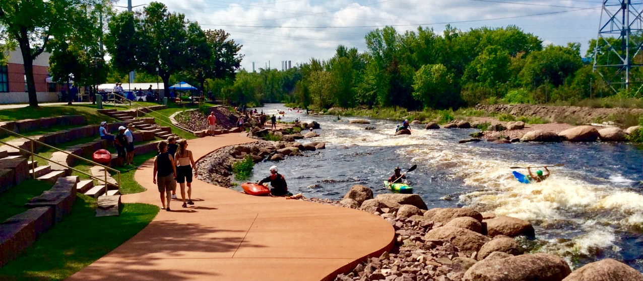 Kayakers paddling the Wisconsin River at Wausau Whitewater Park with spectators along the banks.
